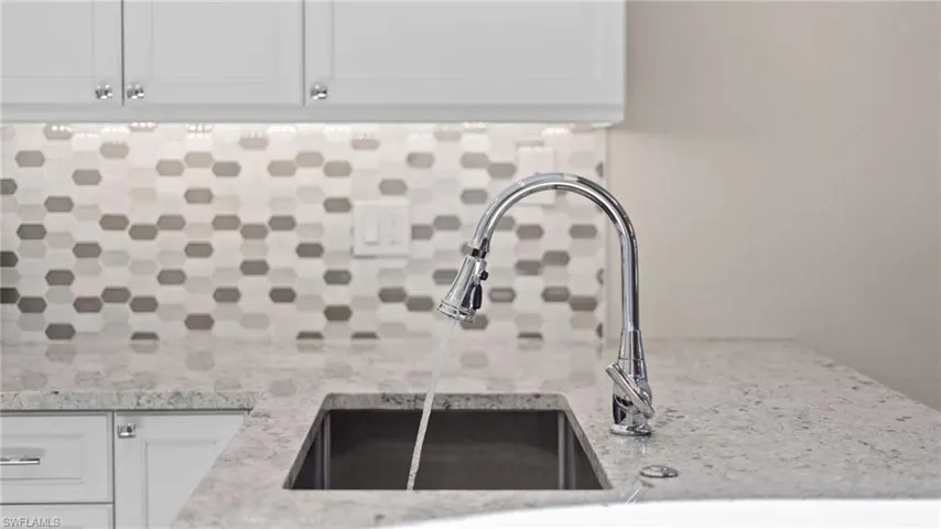 Interior details with white cabinets, backsplash, light stone counters, and sink