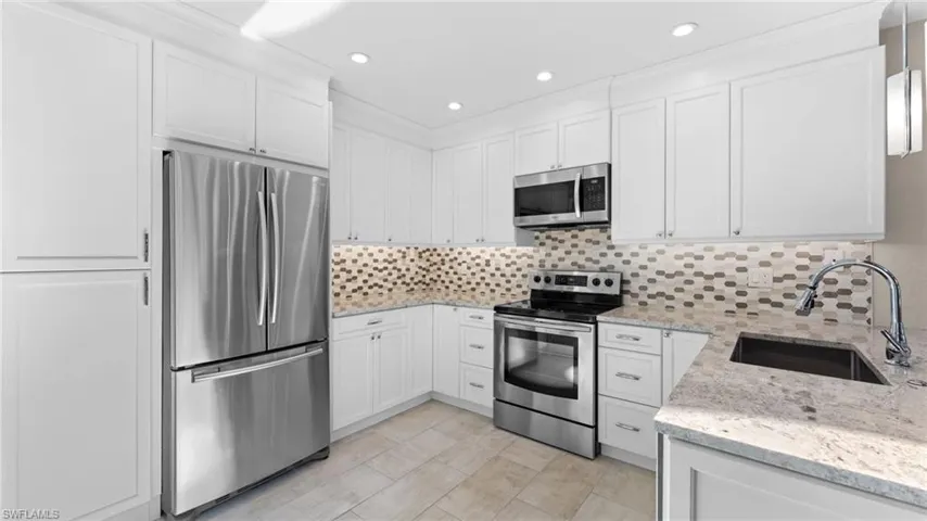 Kitchen with tasteful backsplash, light stone counters, stainless steel appliances, sink, and white cabinetry