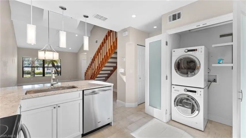 Laundry area with stacked washer / dryer, sink, and light tile patterned floors
