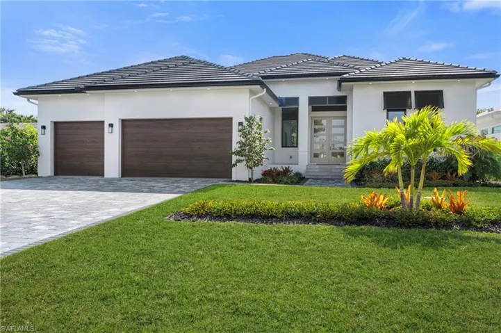 View of front of home with a 3 car garage, a front yard, and french doors