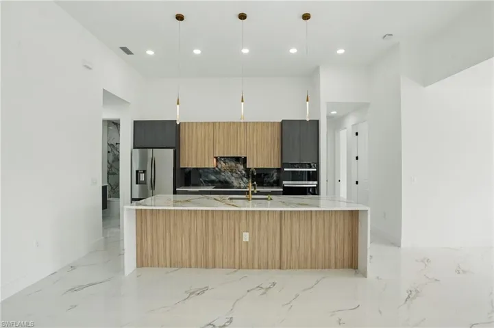 Kitchen with stainless steel refrigerator with ice dispenser, modern cabinets, light marble finish floors, a large island with sink, and baseboards