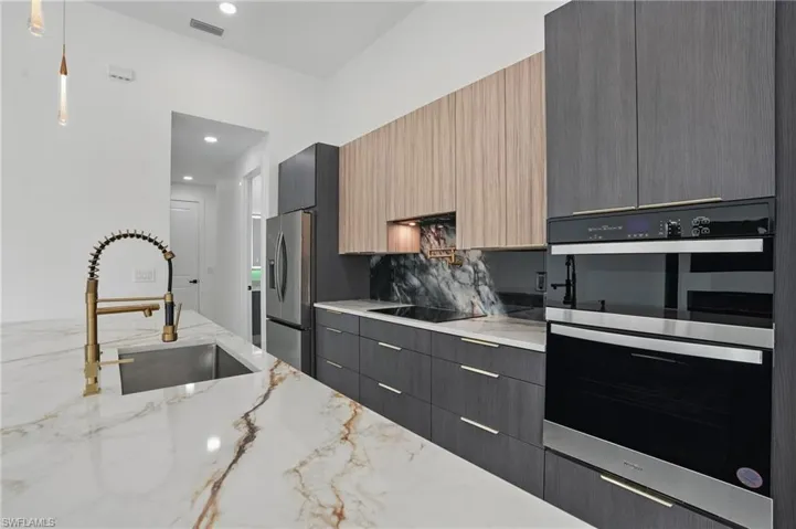 Kitchen with black appliances, a sink, modern cabinets, light stone counters, and decorative light fixtures