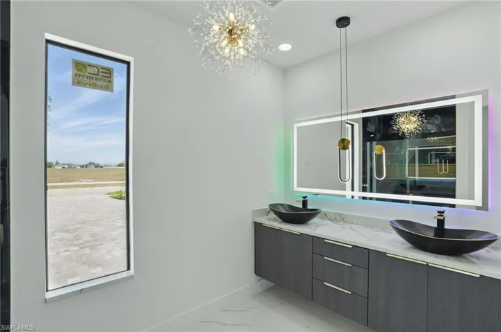 Full bathroom featuring marble look tiles, double vanity, baseboards, and a chandelier