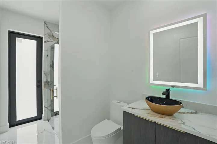 Bathroom featuring a marble finish shower, marble finish flooring, vanity, toilet, and baseboards