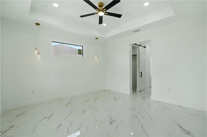 Unfurnished room featuring baseboards, a raised ceiling, recessed lighting, a barn door, and ceiling fan