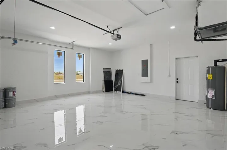 Garage featuring electric panel, a garage door opener, water heater, and recessed lighting
