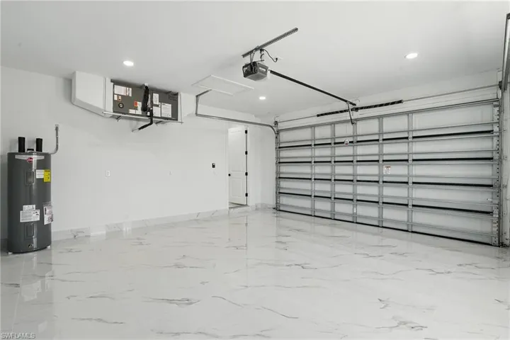 Garage with water heater, a garage door opener, recessed lighting, and baseboards
