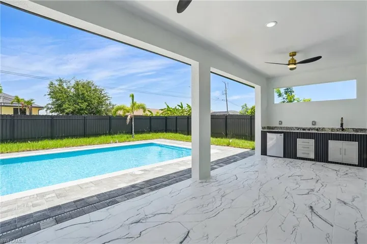 View of swimming pool with ceiling fan, a fenced backyard, exterior kitchen, a patio, and a sink