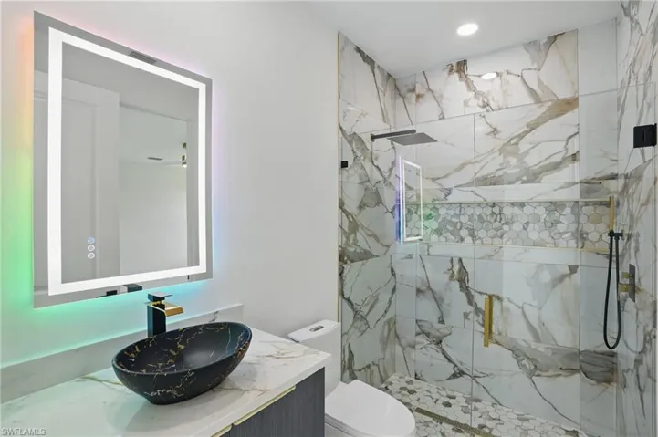 Full bathroom with toilet, a marble finish shower, vanity, and recessed lighting