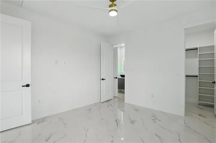 Unfurnished bedroom with baseboards, a spacious closet, marble finish flooring, and a ceiling fan