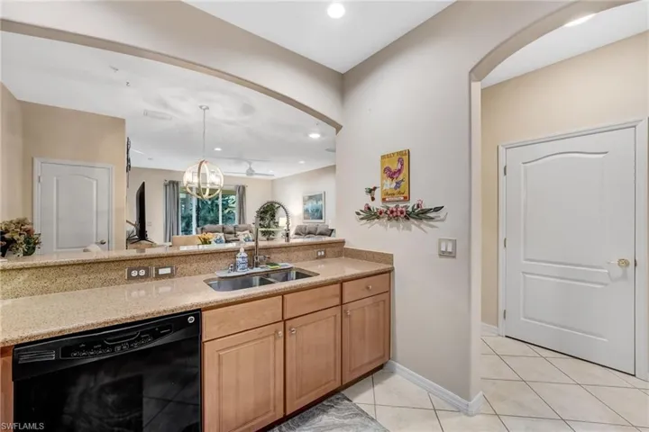 Kitchen with black dishwasher, light stone counters, light tile patterned floors, open floor plan, and wood finish cabinets