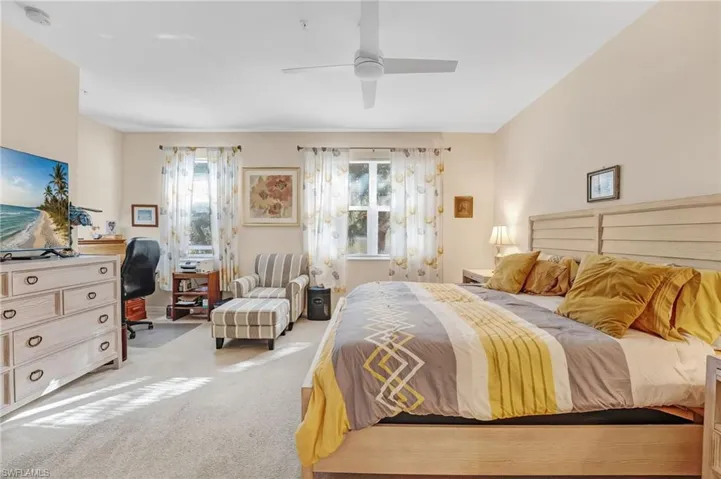 Carpeted bedroom featuring a desk, multiple windows, and ceiling fan