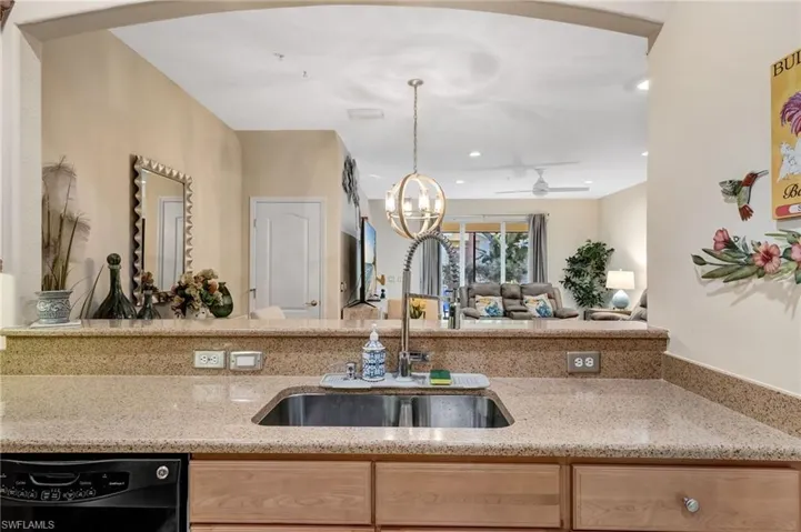 Kitchen featuring light wood finish cabinetry, light stone counters, a ceiling fan, dishwasher, and hanging lights