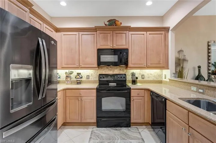 Kitchen featuring black appliances, light stone counters, light tile patterned flooring, backsplash, and recessed lighting