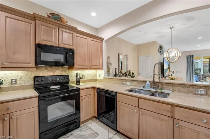 Kitchen featuring black appliances, light stone counters, light tile patterned flooring, and light wood finish cabinets