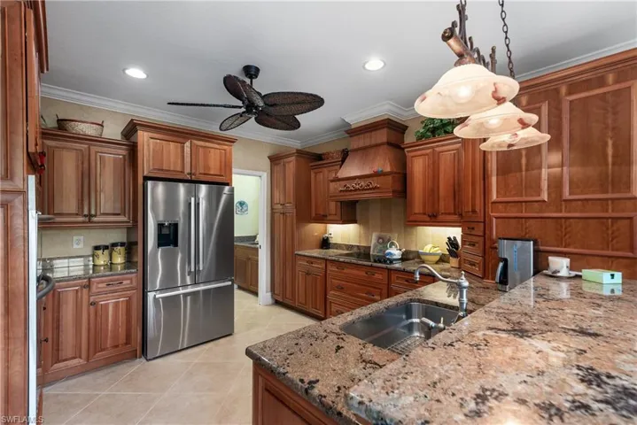 Kitchen with pendant lighting, stainless steel refrigerator with ice dispenser, dark stone counters, sink, and ornamental molding
