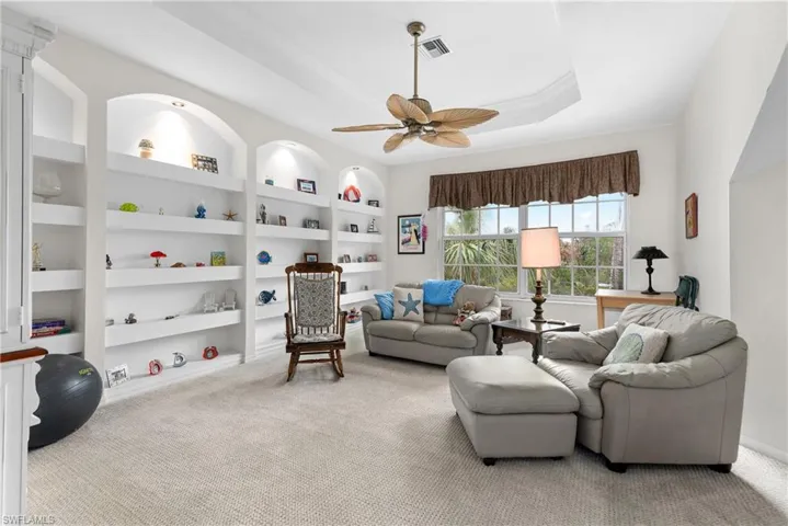 Living room featuring light carpet, built in features, ceiling fan, and a raised ceiling