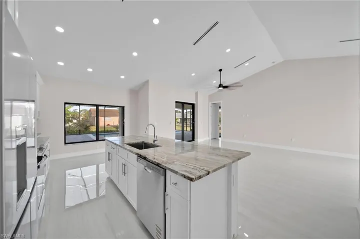 Kitchen featuring stainless steel dishwasher, white refrigerator with ice dispenser, a wealth of natural light, a sink, and lofted ceiling