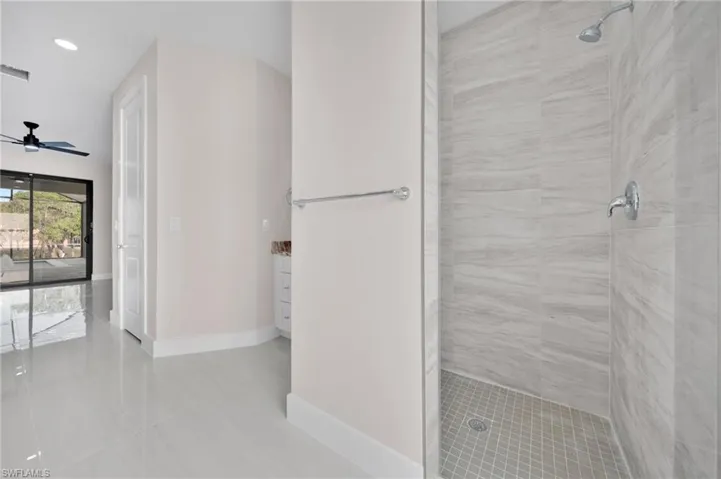 Bathroom with vanity, a tile shower, a ceiling fan, baseboards, and tile patterned flooring