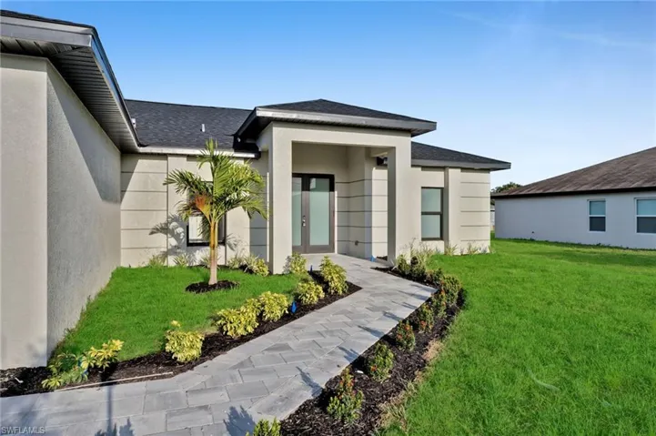 View of exterior entry featuring a lawn, a shingled roof, stucco siding, and french doors