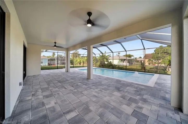Outdoor pool with ceiling fan, glass enclosure, and a patio area