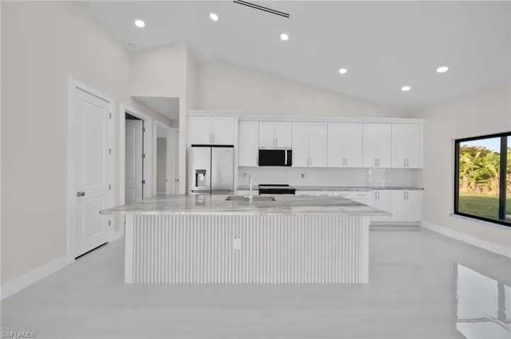 Kitchen featuring a sink, stainless steel appliances, baseboards, vaulted ceiling, and a center island with sink