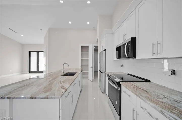 Kitchen with tasteful backsplash, white cabinets, a sink, appliances with stainless steel finishes, and a kitchen island with sink