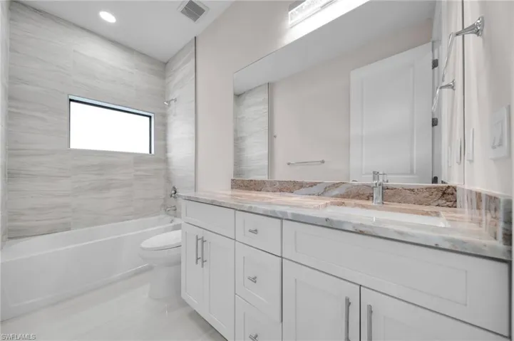 Full bath with a sink, double vanity, visible vents, toilet, and shower / washtub combination