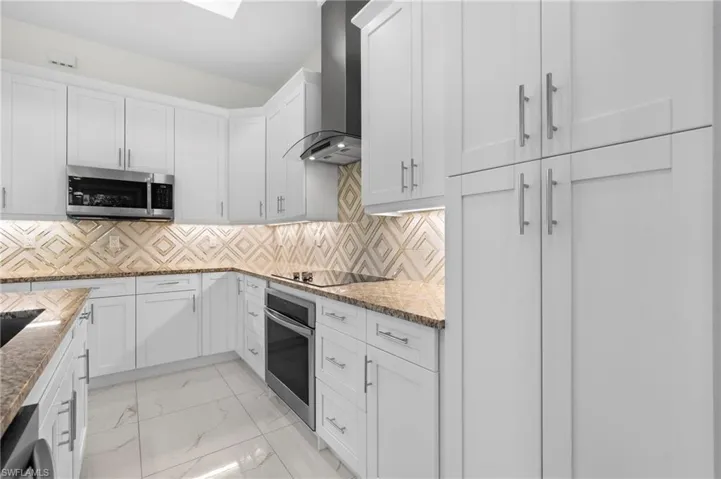 Kitchen with white cabinetry, pantry and geometric design tiled backsplash!