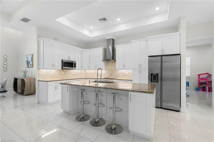 Kitchen featuring wall exhaust hood, state-of-the-art Samsung stainless steel appliances, tan stone countertops, and snack bar!