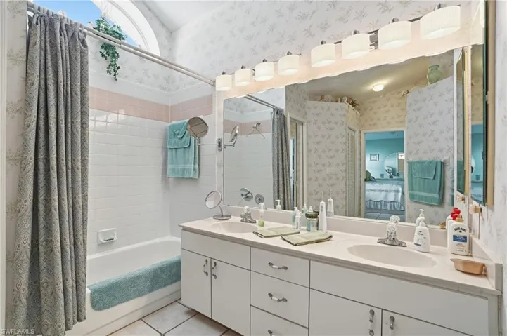 Bathroom with shower / bath combination with curtain, wallpapered walls, double vanity, light tile patterned floors, and connected bathroom