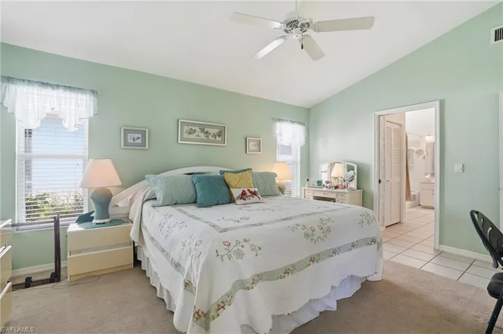 Bedroom featuring vaulted ceiling, ceiling fan, light colored carpet, light tile patterned floors, and ensuite bath