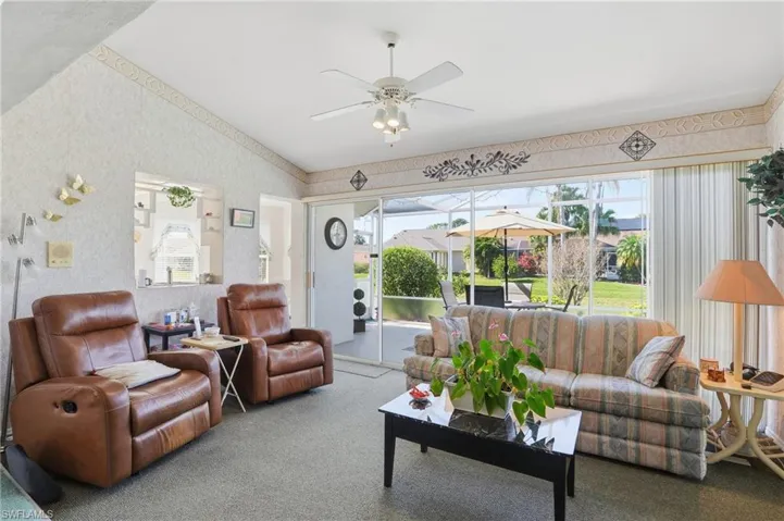 Carpeted living area with a ceiling fan, vaulted ceiling, wallpapered walls, and a sunroom