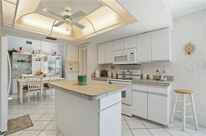 Kitchen featuring white appliances, tile countertops, white cabinetry, ceiling fan, and light tile patterned floors