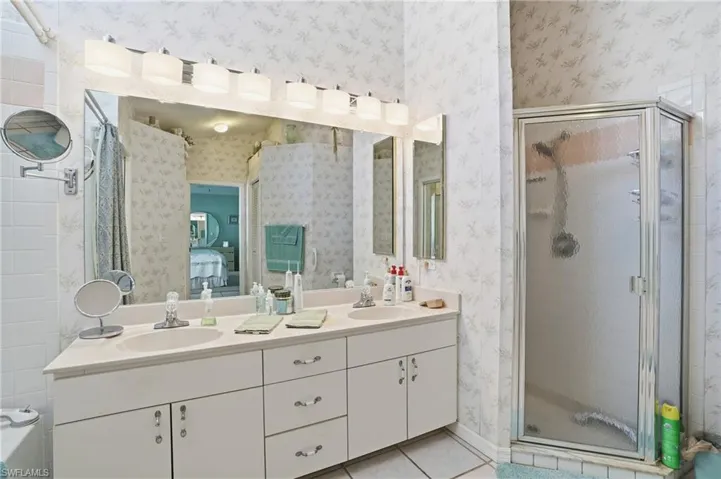 Bathroom with a shower stall, double vanity, light tile patterned floors, connected bathroom, and wallpapered walls