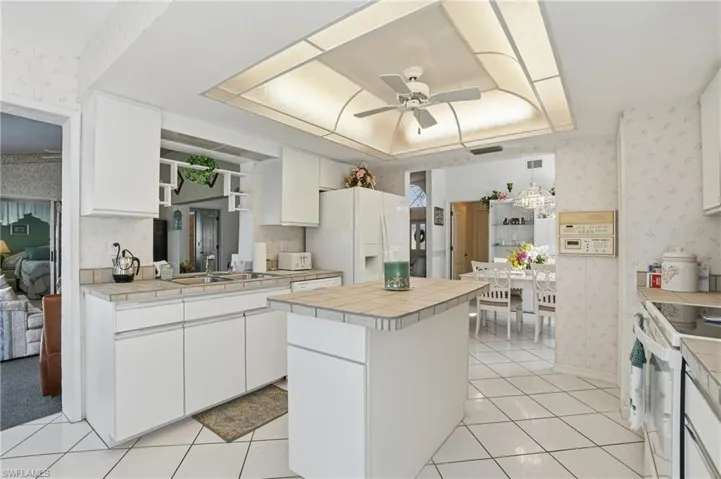Kitchen featuring wallpapered walls, white cabinets, white appliances, tile counters, and ceiling fan