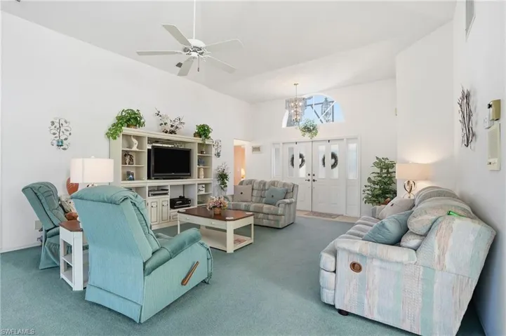 Carpeted living area with high vaulted ceiling, a ceiling fan, and a chandelier