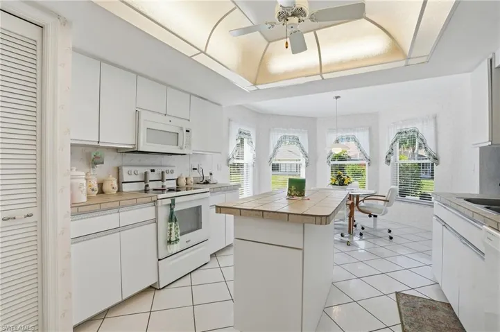 Kitchen with tile counters, white appliances, white cabinets, a ceiling fan, and wallpapered walls