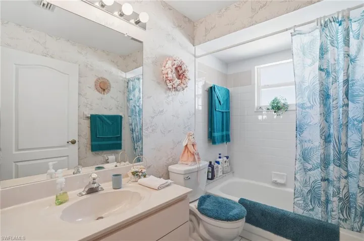 Full bathroom with wallpapered walls, vanity, and shower / tub combo