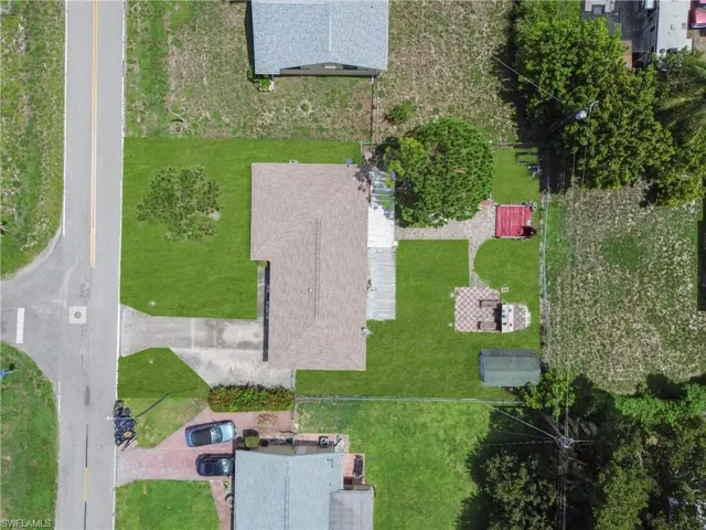 Property featuring a shingle roof, expansive green lawn, paved driveway, and established trees