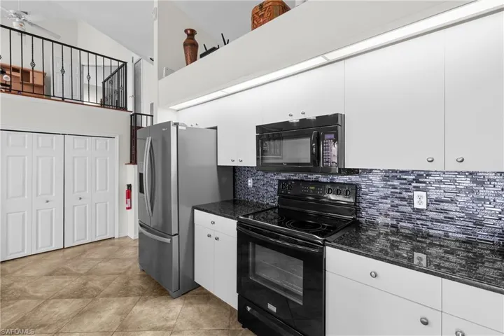 Kitchen featuring backsplash, high vaulted ceiling, black appliances, white cabinets, and ceiling fan