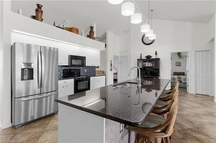 Kitchen featuring sink, black appliances, decorative light fixtures, high vaulted ceiling, and white cabinets