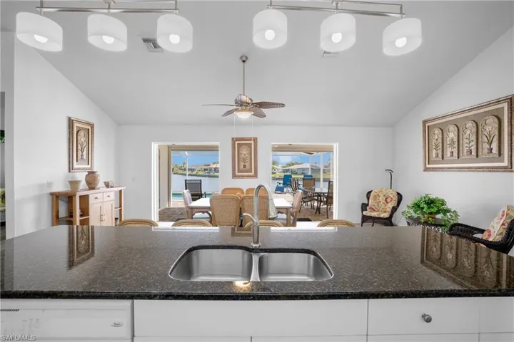 Kitchen featuring sink, dark stone countertops, pendant lighting, lofted ceiling, and white cabinets