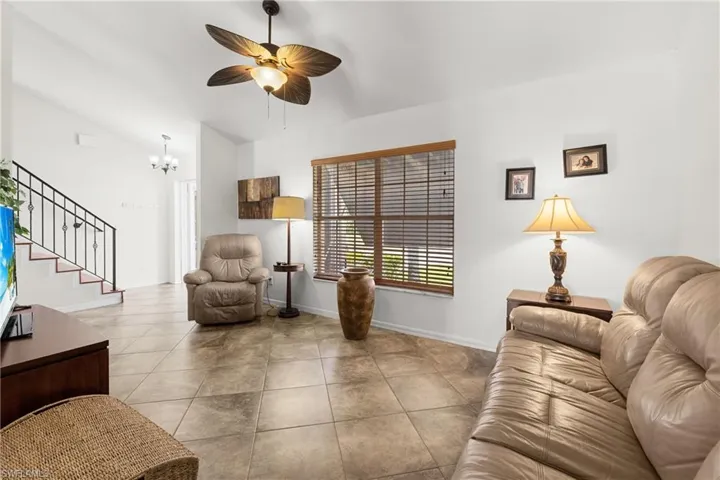 Living room featuring light tile patterned floors, ceiling fan with notable chandelier, and lofted ceiling