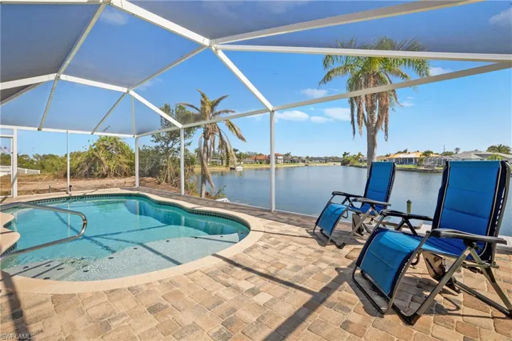 View of pool with glass enclosure, a water view, and a patio