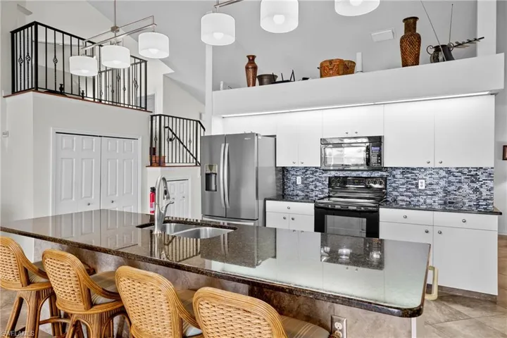 Kitchen featuring pendant lighting, backsplash, a high ceiling, black appliances, and sink