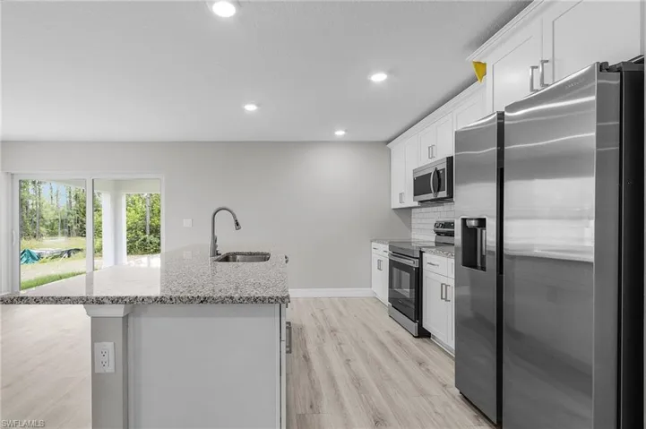 Kitchen with appliances with stainless steel finishes, a sink, a kitchen island with sink, light wood-style floors, and decorative backsplash