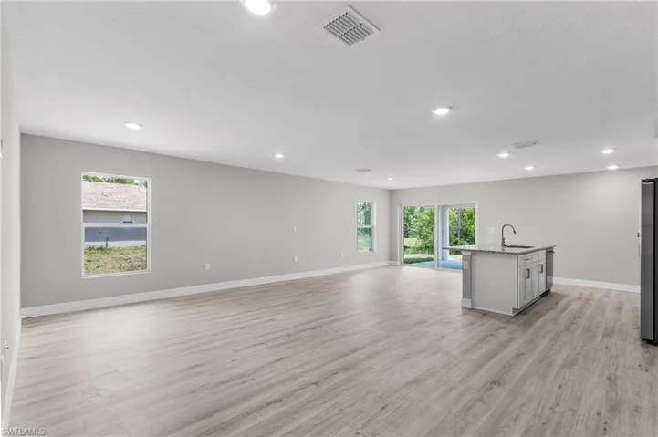 Unfurnished living room with a sink, recessed lighting, light wood-type flooring, and baseboards