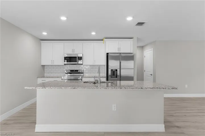 Kitchen featuring stainless steel appliances, a sink, an island with sink, baseboards, and light wood-type flooring