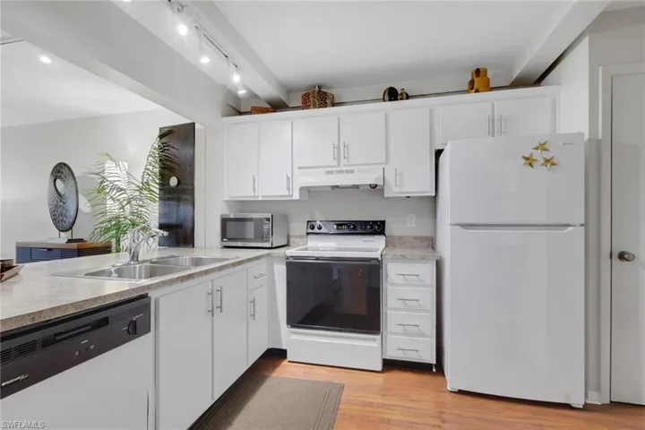 Kitchen with white appliances, light countertops, white cabinetry, and light wood-type flooring